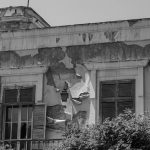 Black and white photo of an old building facade with peeling paint and closed shutters.