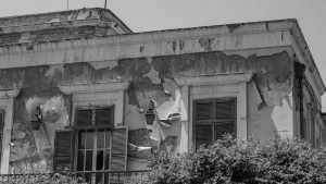 Black and white photo of an old building facade with peeling paint and closed shutters.