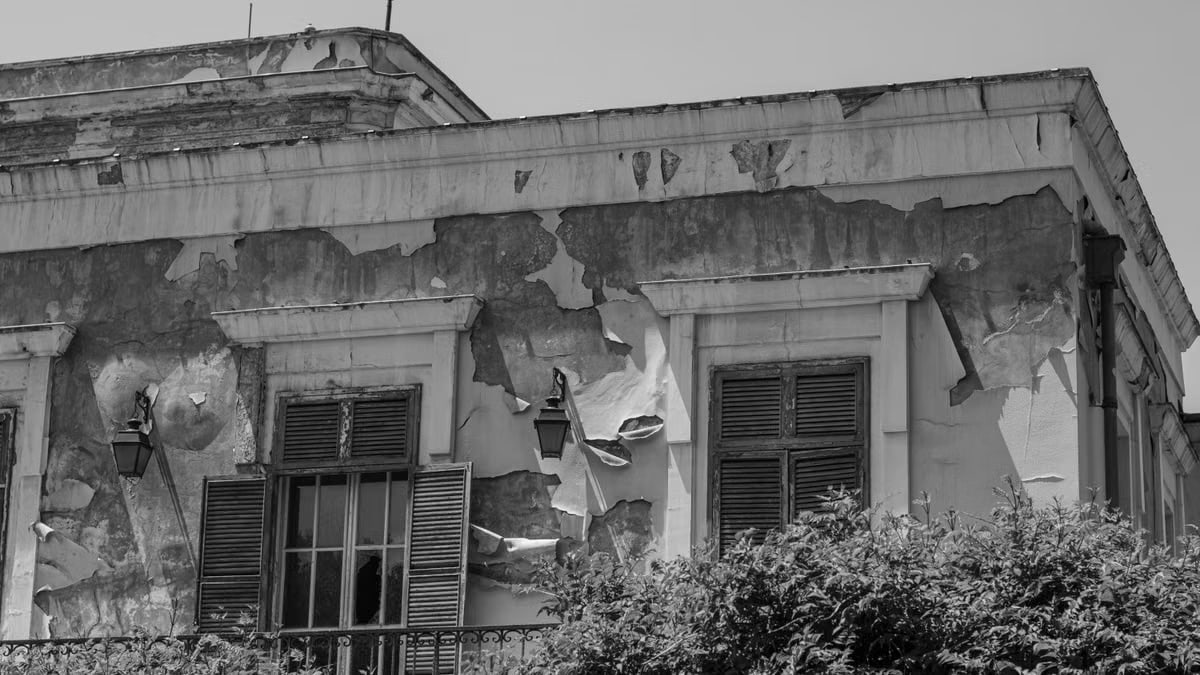 Black and white photo of an old building facade with peeling paint and closed shutters.
