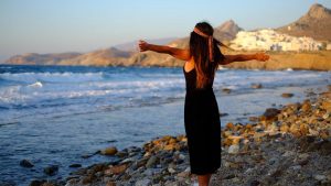 Woman enjoying freedom at sunset on a rocky beach in Greece.