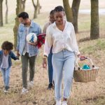 A joyful family walking in a park, carrying a picnic basket and a ball on a sunny day.